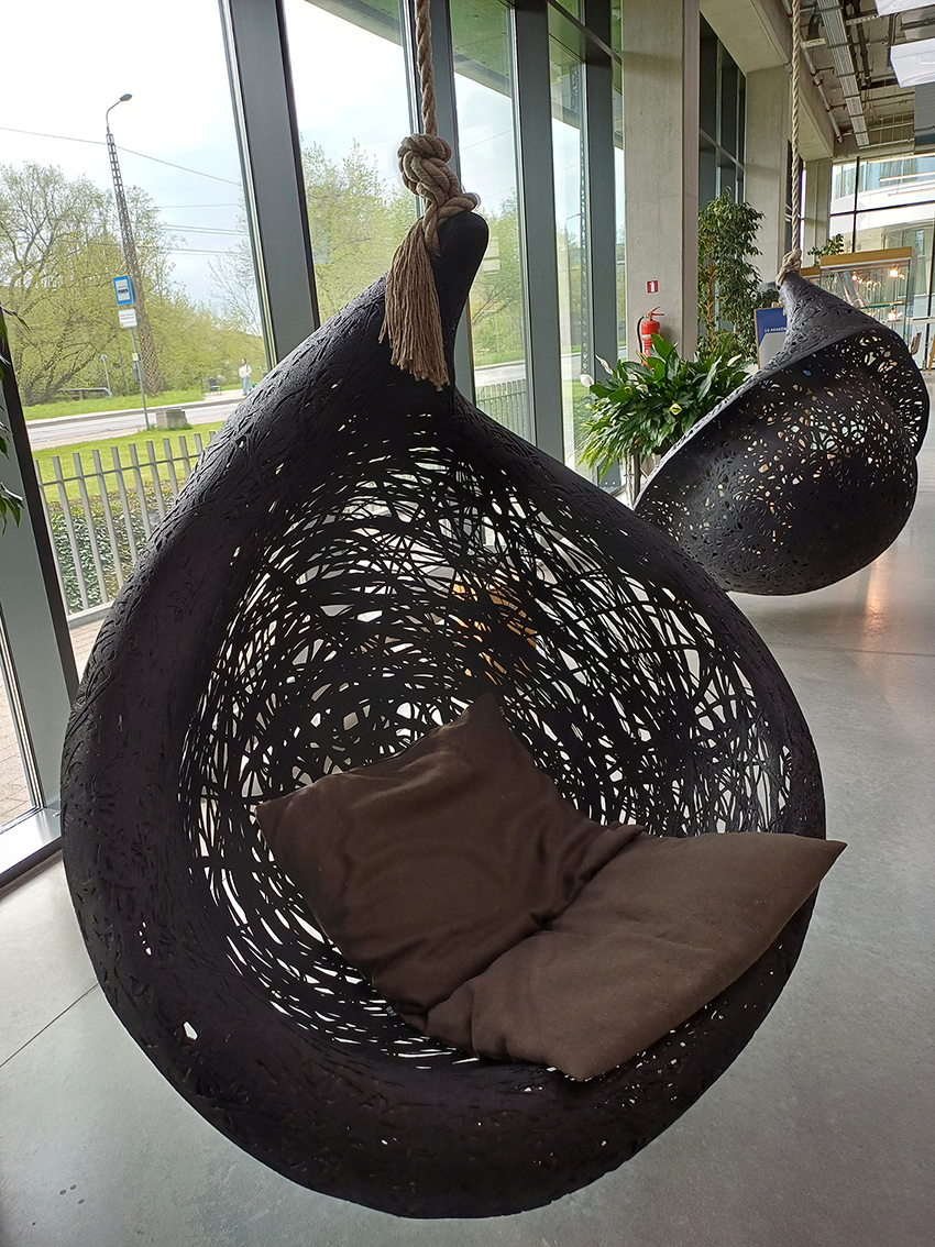 Das Bild zeigt zwei Hängesessel aus einem dunklen Material vor einer Fensterfront mit Blick auf eine Straße. 