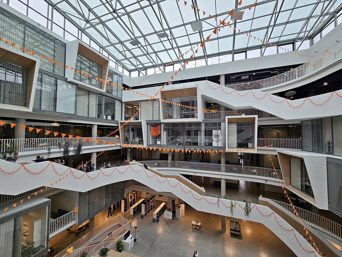 Die Abbildung zeigt das Atrium im House of Science der Universität Riga. Durch den Raum und über die weißen Treppen ziehen sich orangefarbene Wimpelketten. 