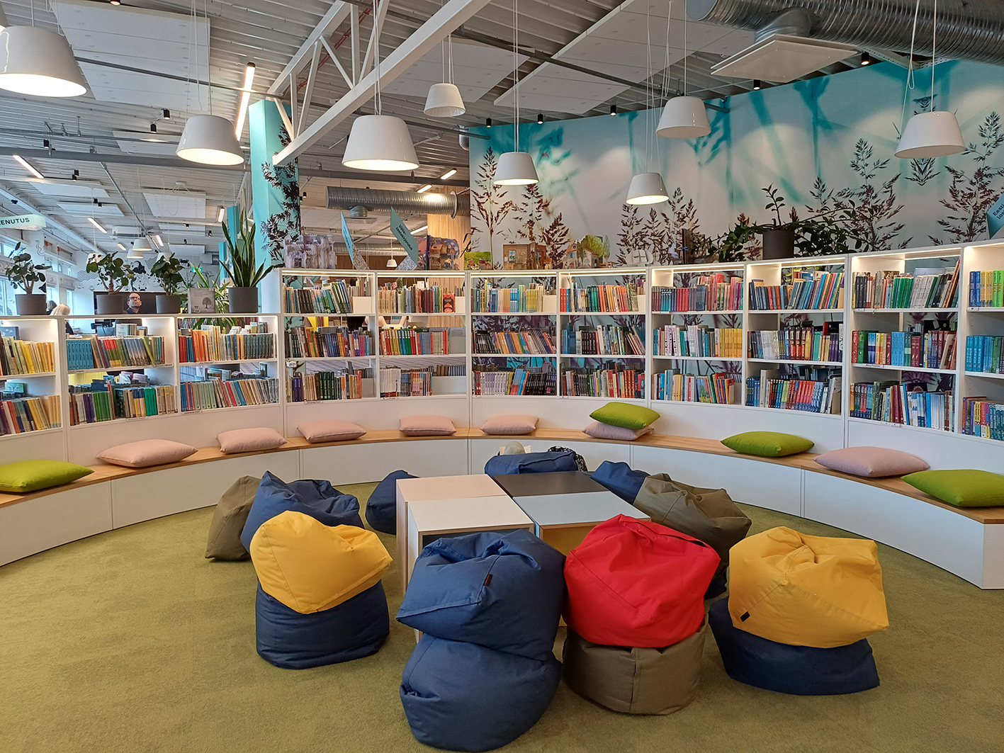 Ein bunter Kinderbereich mit Sitzkissen und einem geschwungenen, halbhohen Regal in  der Stadtbibliothek Viimsi. 