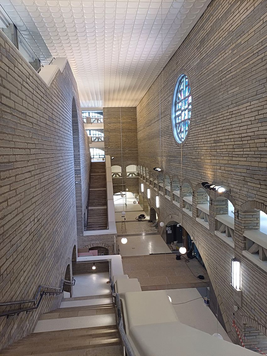 Die Abbildung zeigt den Eingangsbereich der estnischen Nationalbibliothek aus dem Obergeschoss. Es sind mehrere Treppen sowie ein rundes, buntes Glasfenster zu sehen. 