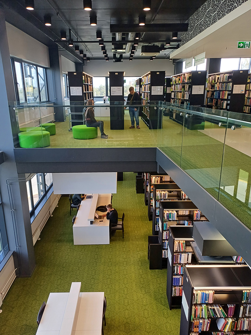 Die Abbildung zeigt zwei Etagen der Lesesäle in der TalTech-Bbliothek.  Es sind Bücherregale und Arbeitsplätze zu sehen. Die vorherrschende Farbe ist grün. 