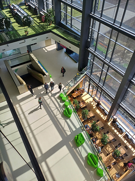 Die Abbildung zeigt den Eingangsbereich der estnischen Nationalbibliothek aus dem Obergeschoss. Es sind mehrere Treppen sowie ein rundes, buntes Glasfenster zu sehen. 