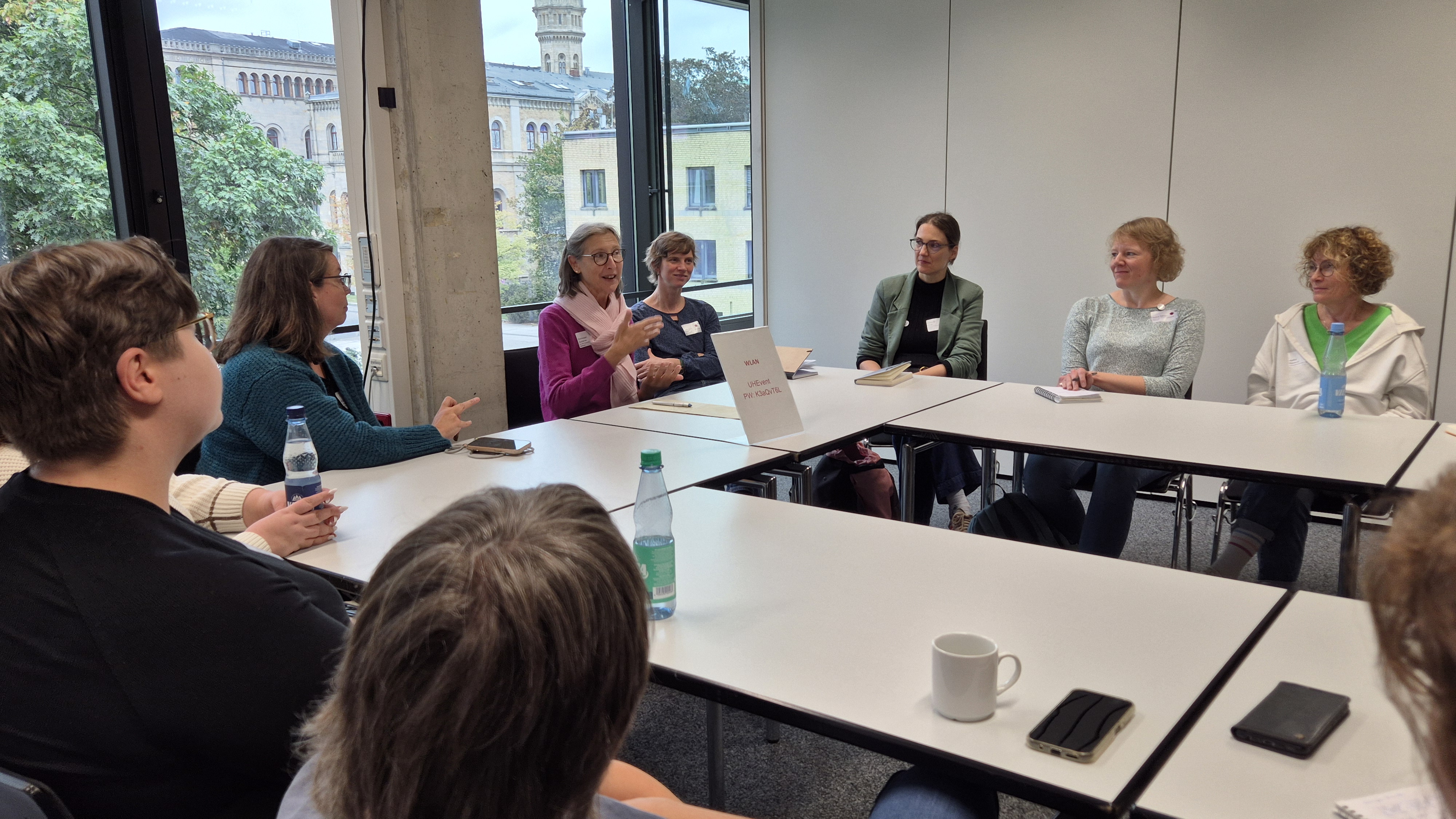 <i>Teilnehmende einer Session, Foto: TIB / A. Bätje</i> Teilnehmende um U-förmig angeordnete Tische. Etwa 10 Personen sind im Gespräch, eine Person gestikuliert, die anderen hören zu.