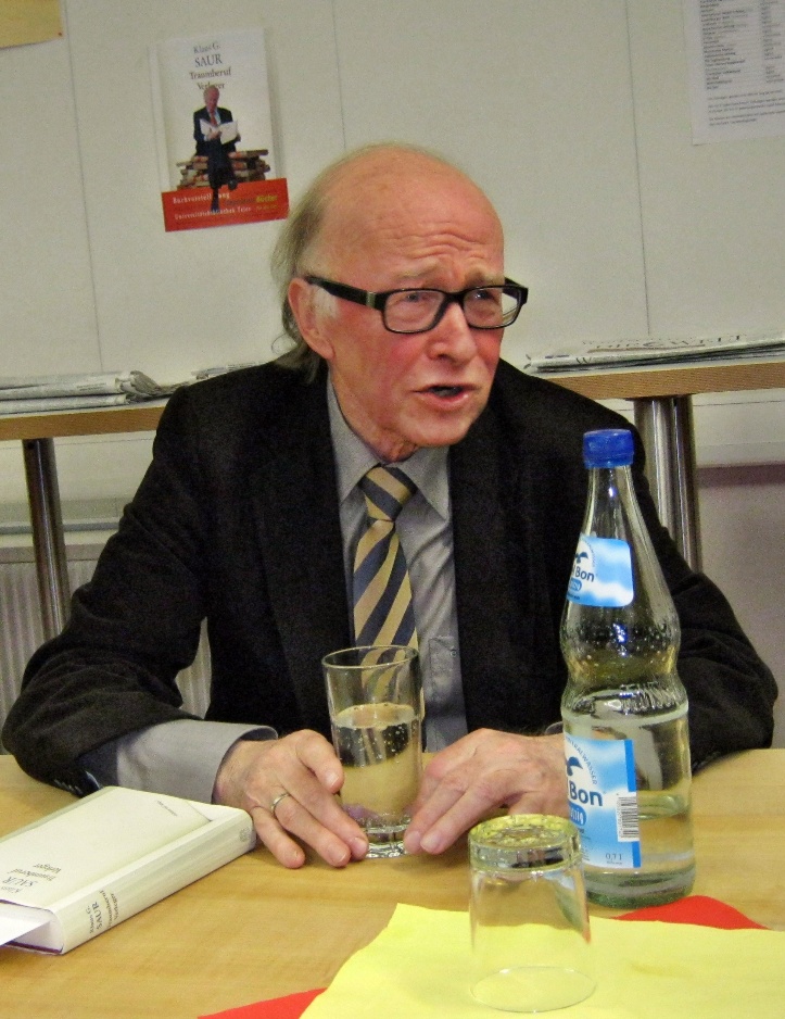 Klaus G. Saur im Jahr 2011. Foto: Wikimedia Commons (CC0) Foto von Klaus G. Saur an einem Tisch sitzend, vor sich ein Glas Wasser und ein Buch.